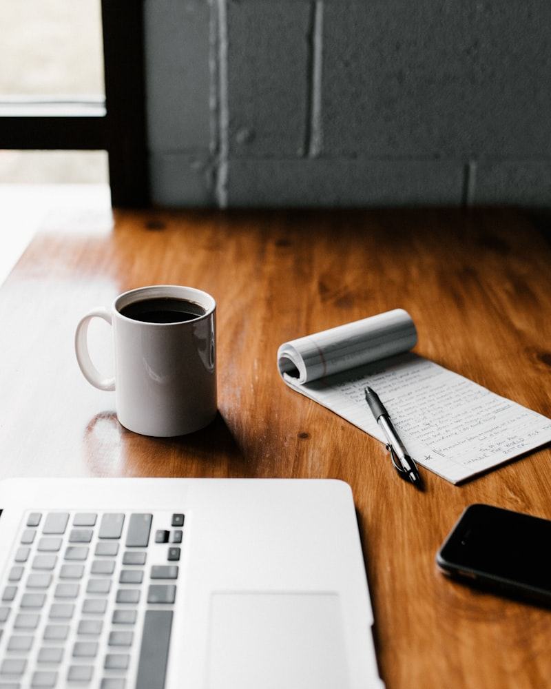 A notebook, pen and coffee cup on a wooden desk